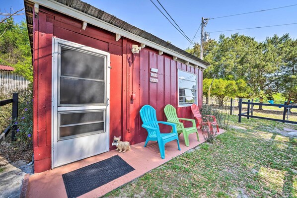 Un bâtiment rouge avec une grande porte-fenêtre coulissante, deux fauteuils Adirondack et un petit chien sur le porche.