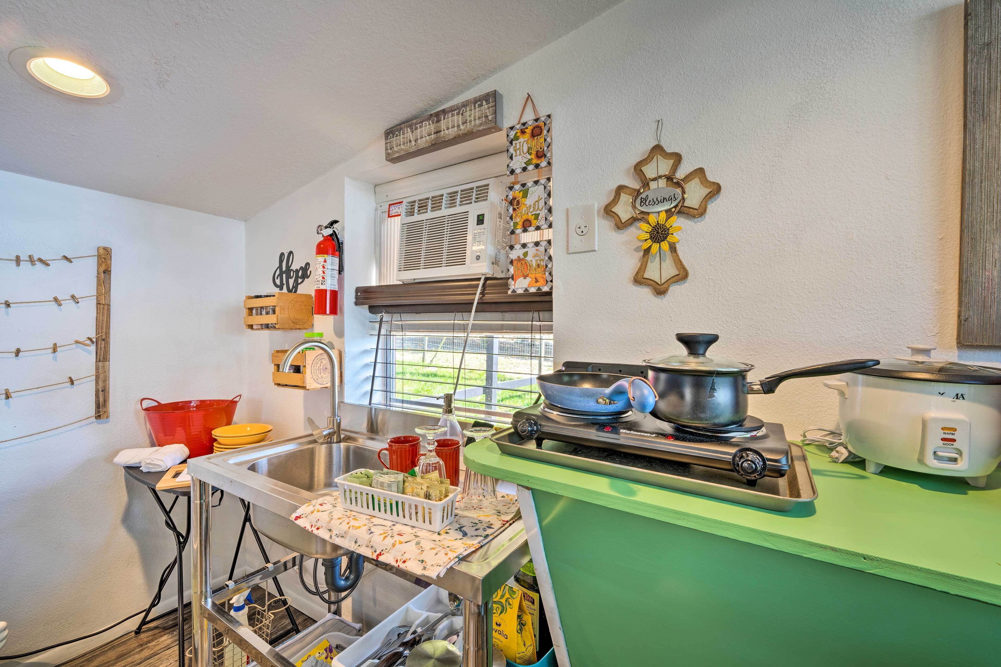 A kitchen with a stove, sink, and various kitchen items. There is a window with blinds and a wall-mounted air conditioner.