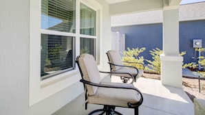 Un patio couvert avec deux chaises et une table, une fenêtre avec des stores et un mur bleu en arrière-plan.