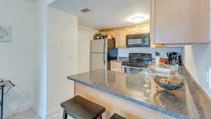 A modern kitchen with granite countertops, stainless steel appliances, wooden cabinets, and a breakfast bar.