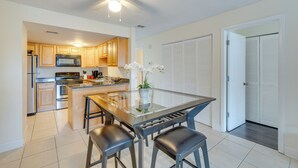A modern kitchen with wooden cabinets, a stainless steel refrigerator, a microwave, and a glass-top dining table with four chairs.