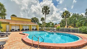 A swimming pool with a brick deck, lounge chairs, and a building with yellow walls in the background.