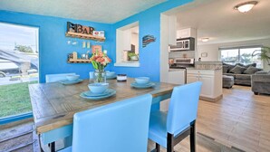 Un comedor con una mesa de madera y sillas azules, una cocina al fondo y una pared azul de acento.