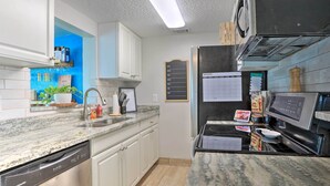 Una cocina moderna con armarios blancos, encimera de granito, lavavajillas, refrigerador y un calendario en la pared.