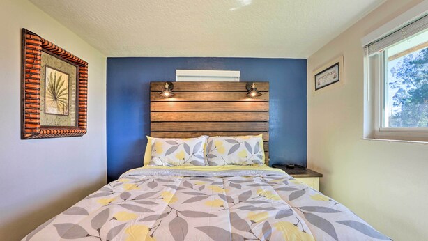 Un dormitorio con cama, cabecera con luces, ventana y un cuadro enmarcado en la pared.