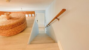 Een houten trap met een geweven poef en een houten leuning.