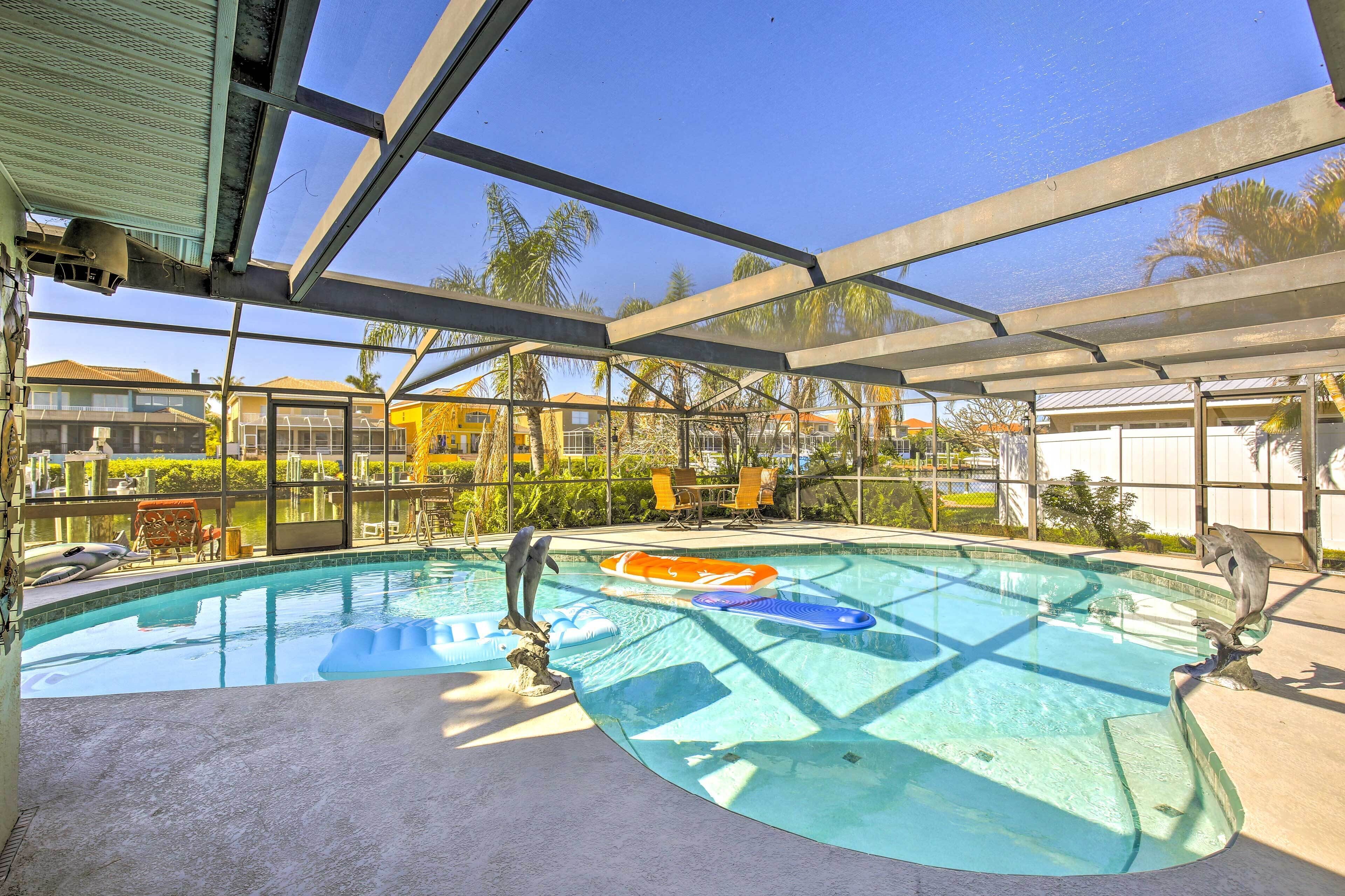 Une piscine entourée d’une paroi en verre, avec des chaises et un palmier tout autour.