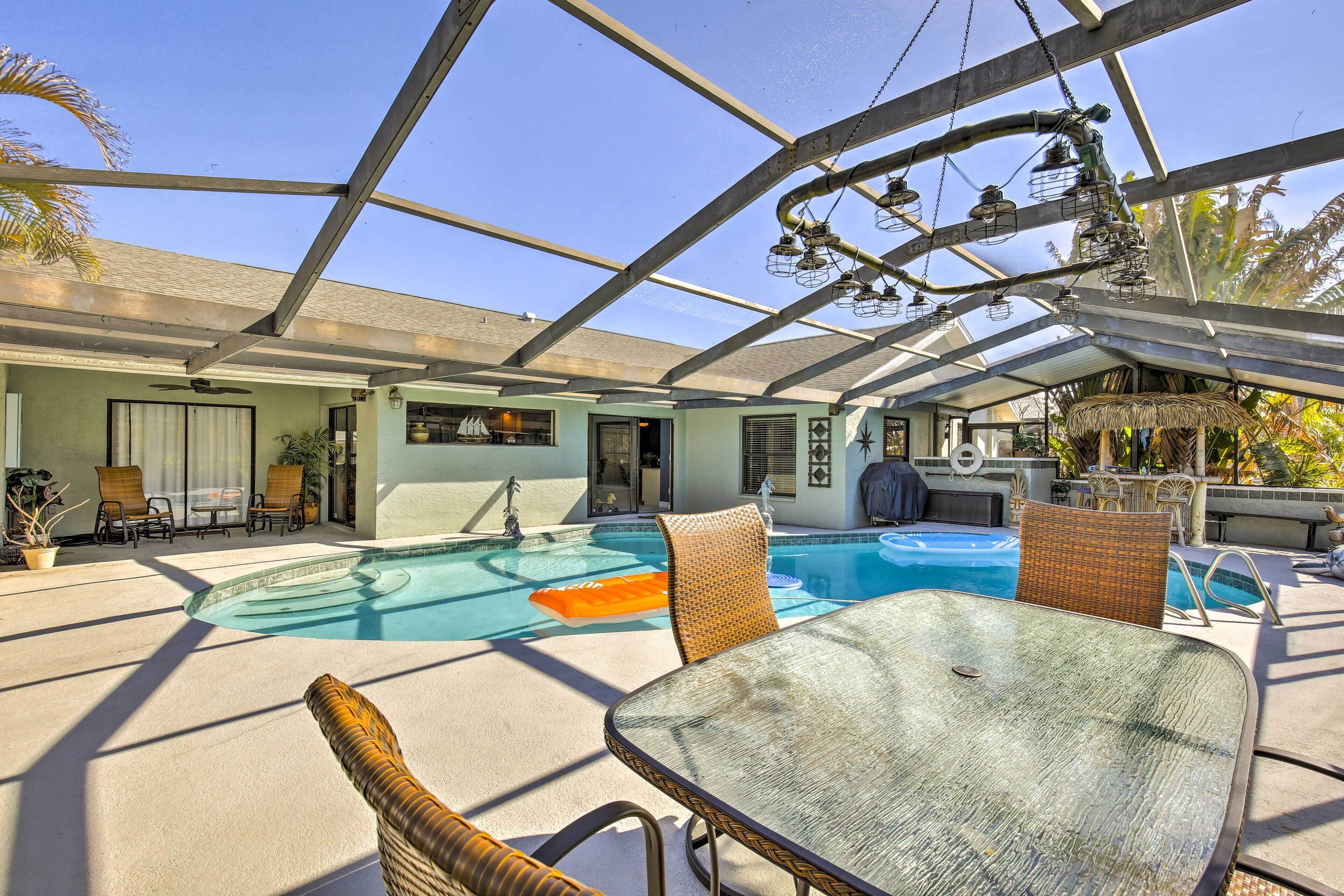 Zona de piscina exterior techada con sillones de descanso y una mesa, rodeada por un recinto de vidrio.
