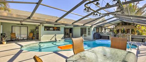 Zona de piscina exterior techada con sillones de descanso y una mesa, rodeada por un recinto de vidrio.
