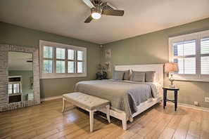 A bedroom with a bed, bench, ceiling fan, and large windows.