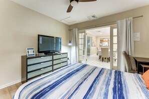 Un dormitorio con cama, televisor sobre una cómoda y vista a la cocina por una puerta abierta.