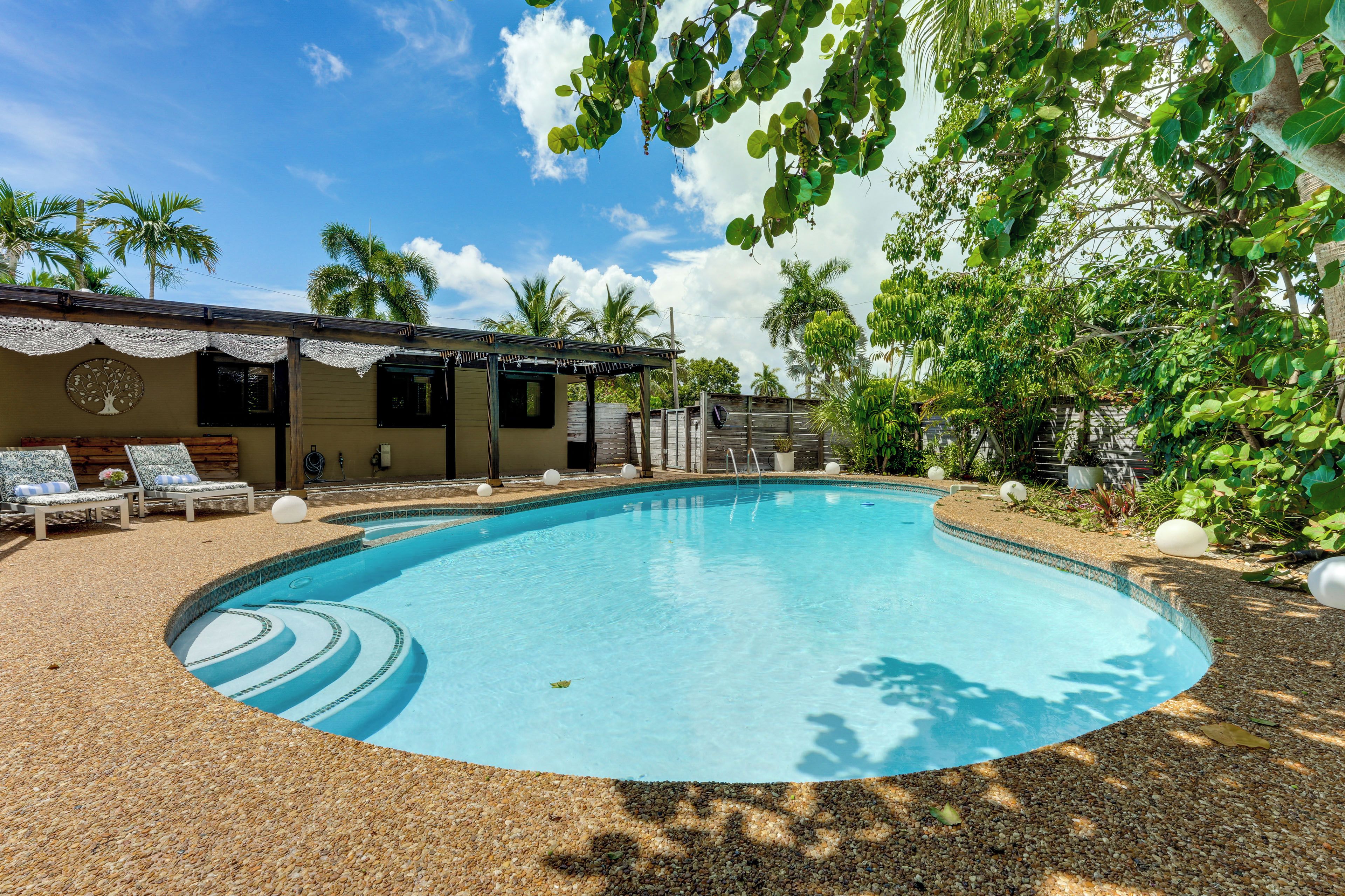 Una piscina con borde de azulejos, rodeada de sillas de descanso y una zona de estar cubierta.