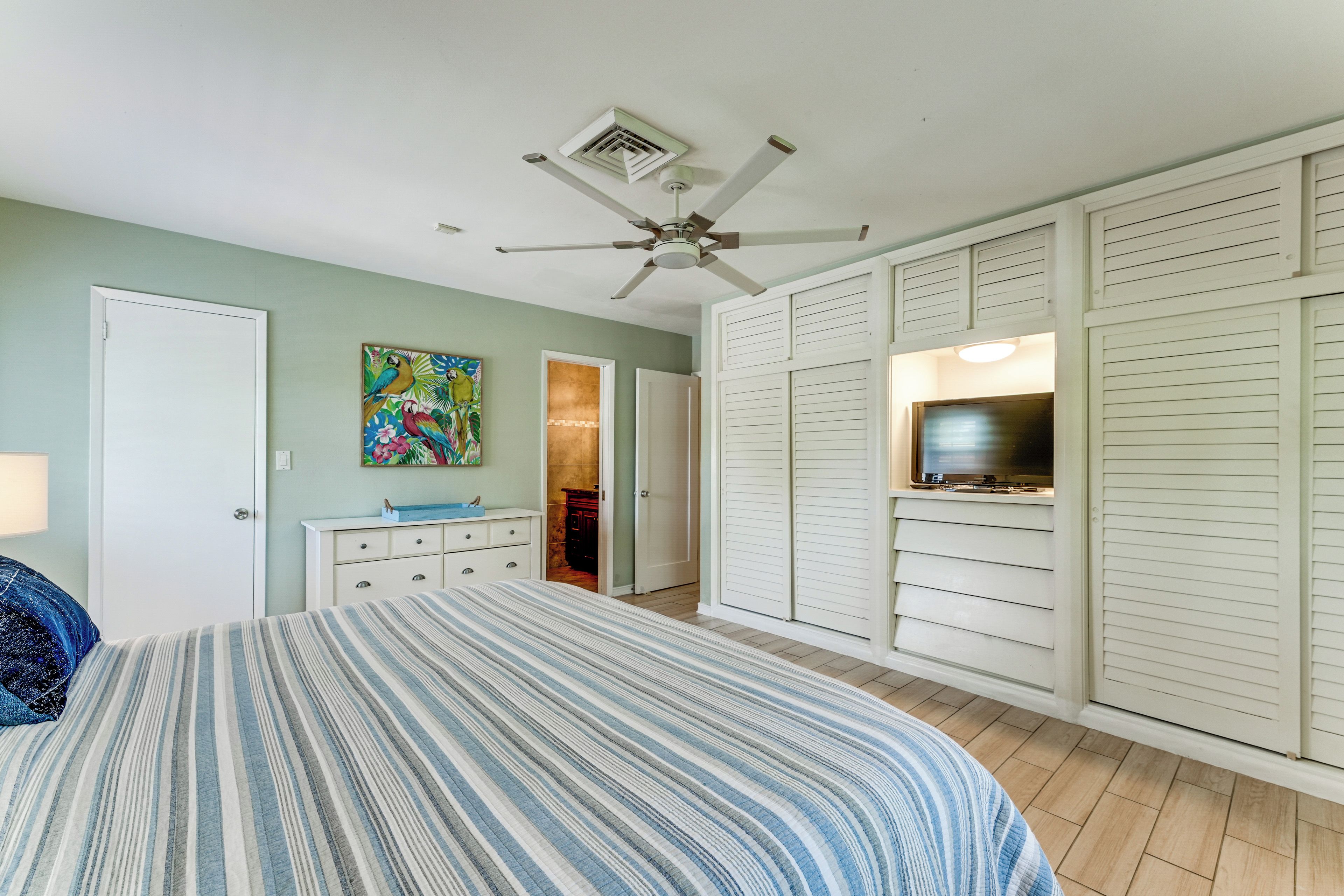 A bedroom with a bed, a ceiling fan, a TV, and a closet with sliding doors.