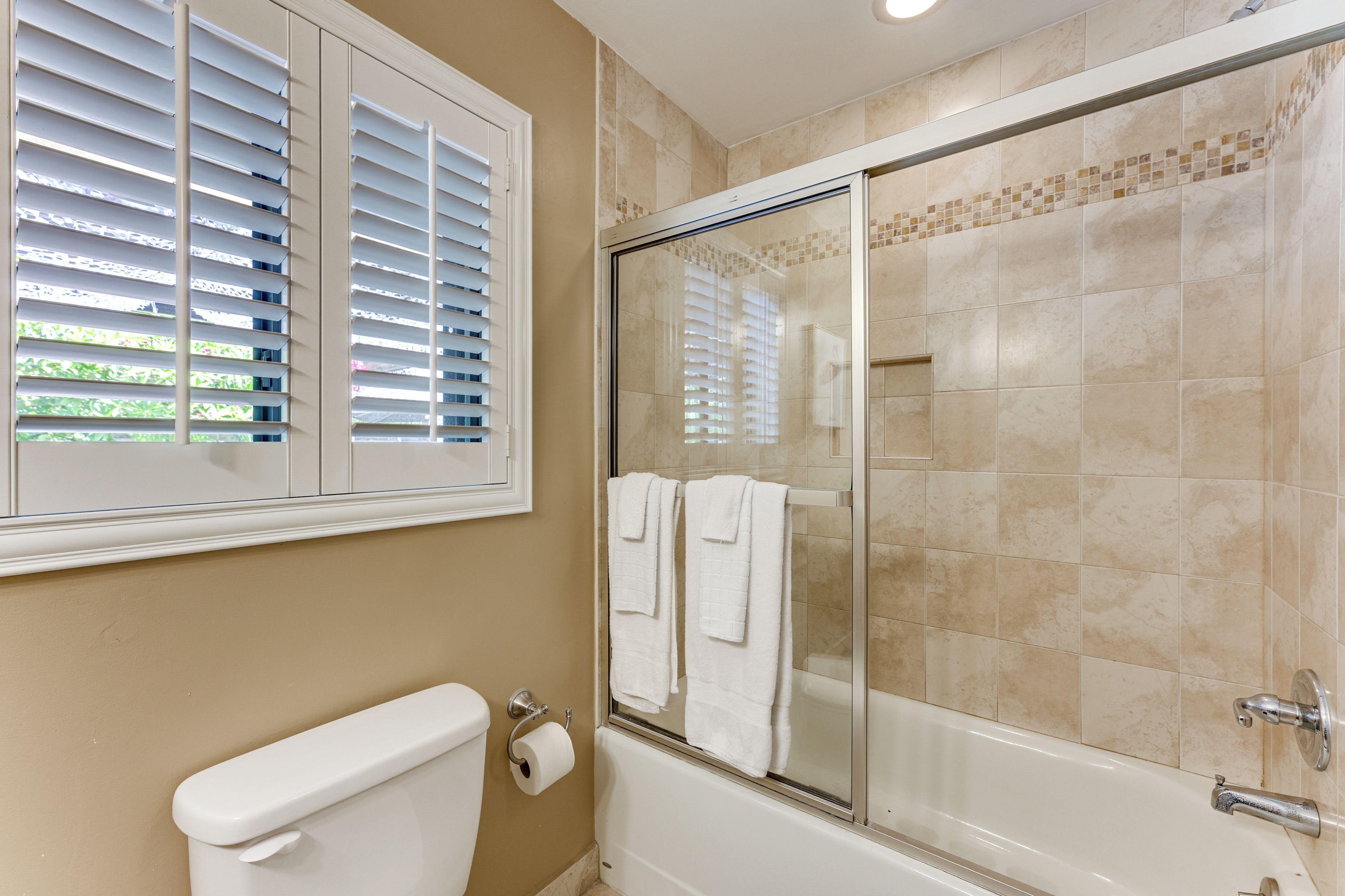 A bathroom with a toilet, a glass-enclosed shower, and a window with blinds.