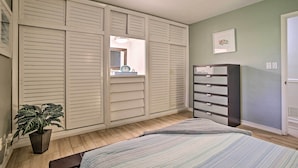 Ein Schlafzimmer mit Bett, Kommode, Blumentopf und Schrank mit Schiebetüren.