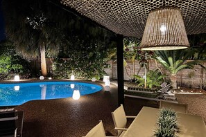 A pool area with a curved edge, surrounded by chairs and tables, under a canopy with a woven design. - 2 Mi to Beach! Oakland Park Home w/ Outdoor Oasis (Oakland Park)
