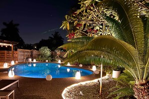 Piscina rodeada de plantas e iluminación nocturna.