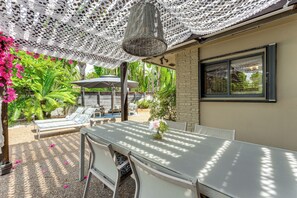 Une terrasse avec une table et des chaises, un parasol en osier et une vue sur une piscine et de la verdure.