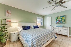 Un dormitorio con cama, mesitas de noche, cómoda, ventilador de techo, ventana con persianas y decoración en la pared.