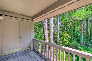 A wooden deck with a white railing, overlooking a forested area with tall trees.