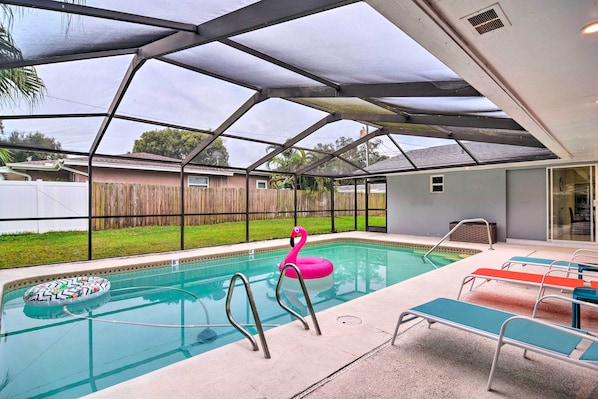 A covered swimming pool with a pink flamingo float, a ladder, and lounge chairs.