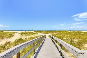 A wooden boardwalk leading to a beach with dunes and a clear sky.