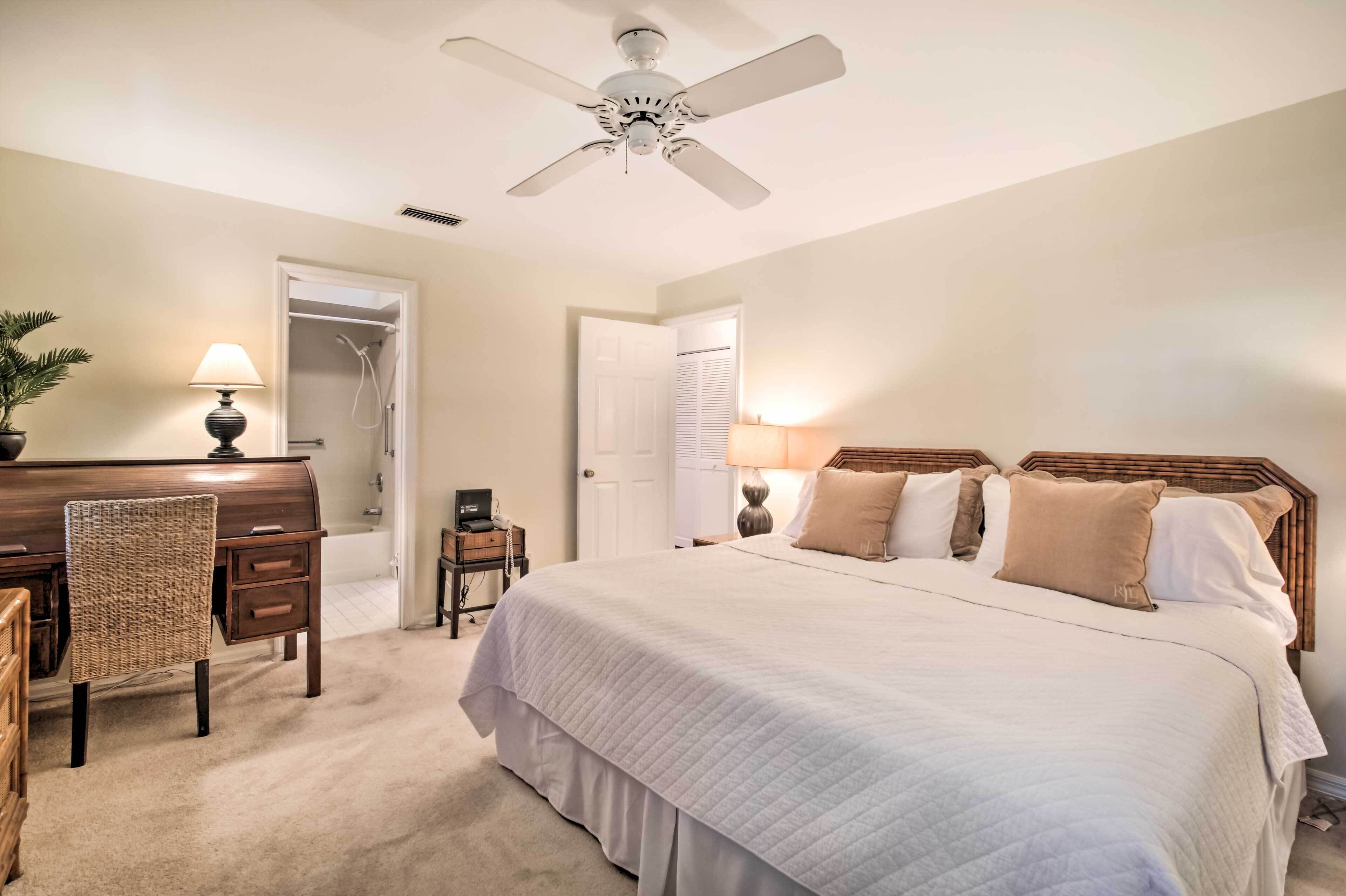 A bedroom with a large bed, a desk with a lamp, a ceiling fan, and a closet.