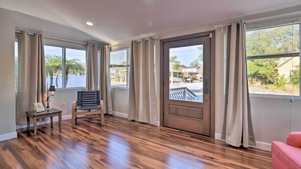 A spacious room with hardwood flooring, large windows with curtains, a door with a view, and a chair. - Vibrant Dunedin Getaway w/ Furnished Patio! (Dunedin)