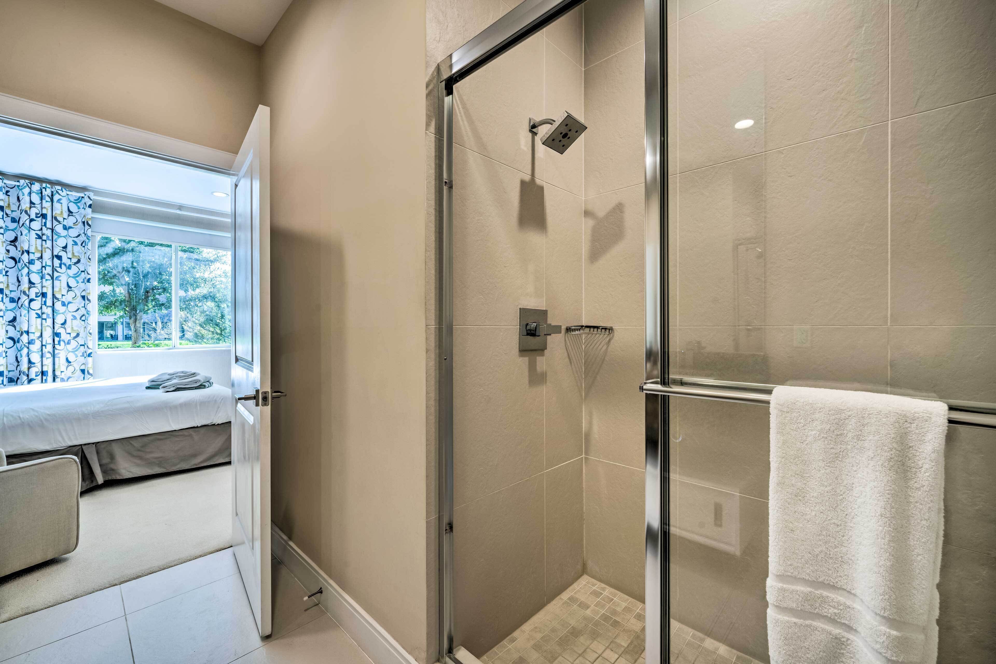 A modern bathroom with a glass shower enclosure, a white towel hanging on the wall, and a window with a view of greenery.