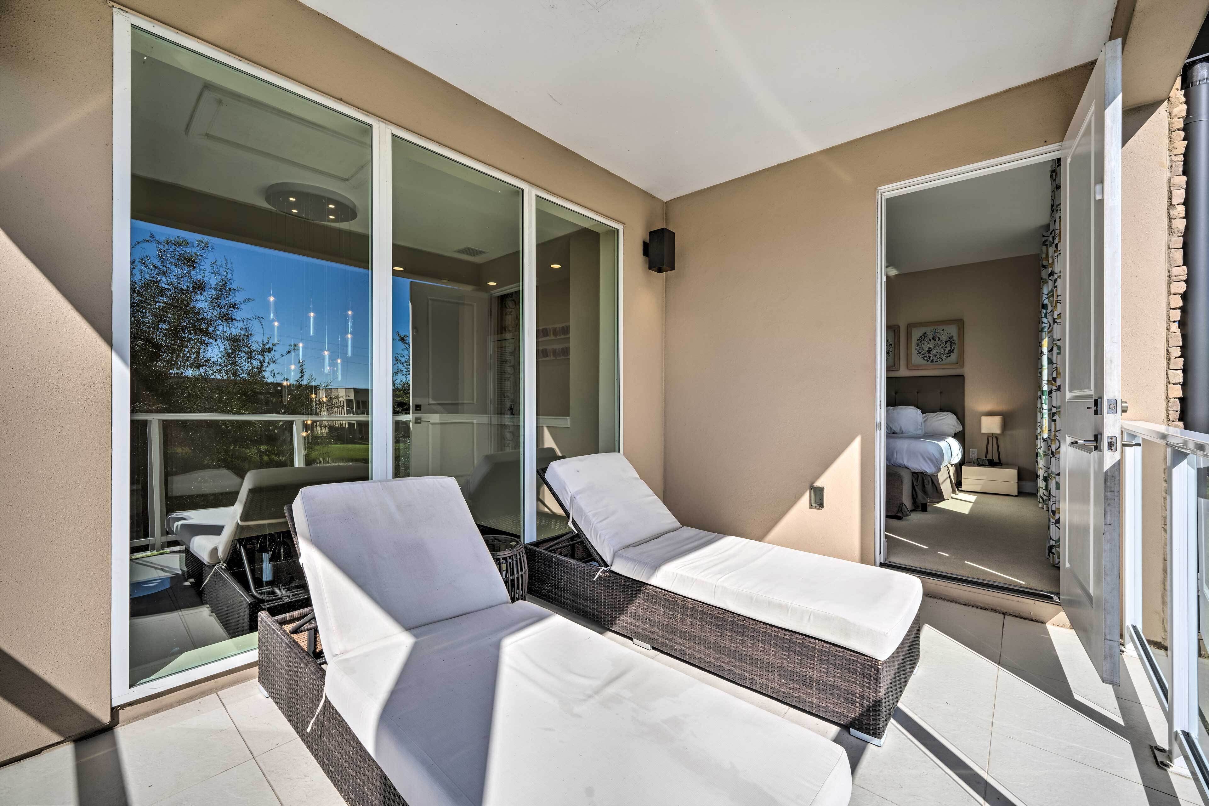 A balcony with two sun loungers and a glass door leading to a bedroom.