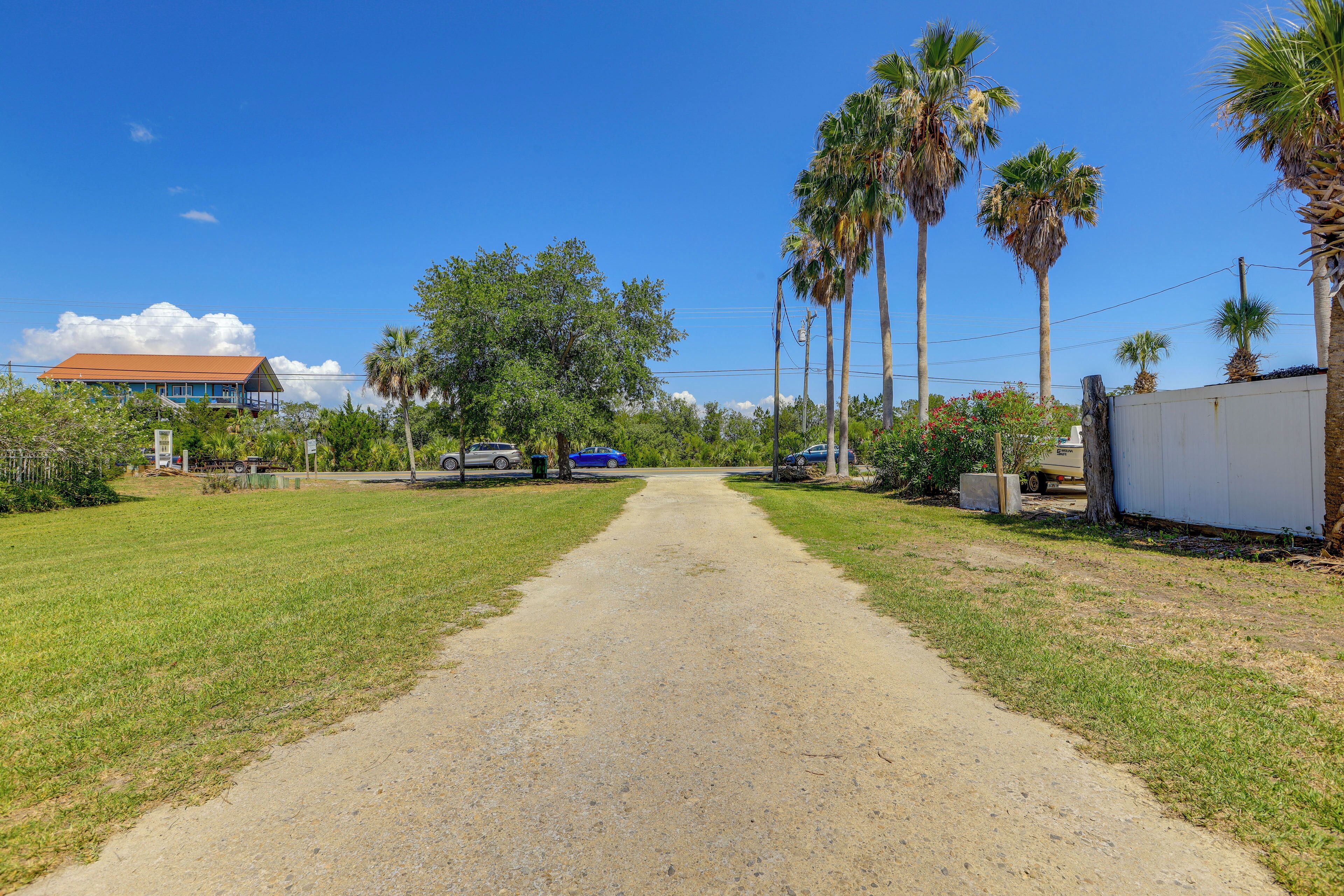 A gravel path leading to a house with a red roof, surrounded by palm trees and greenery.