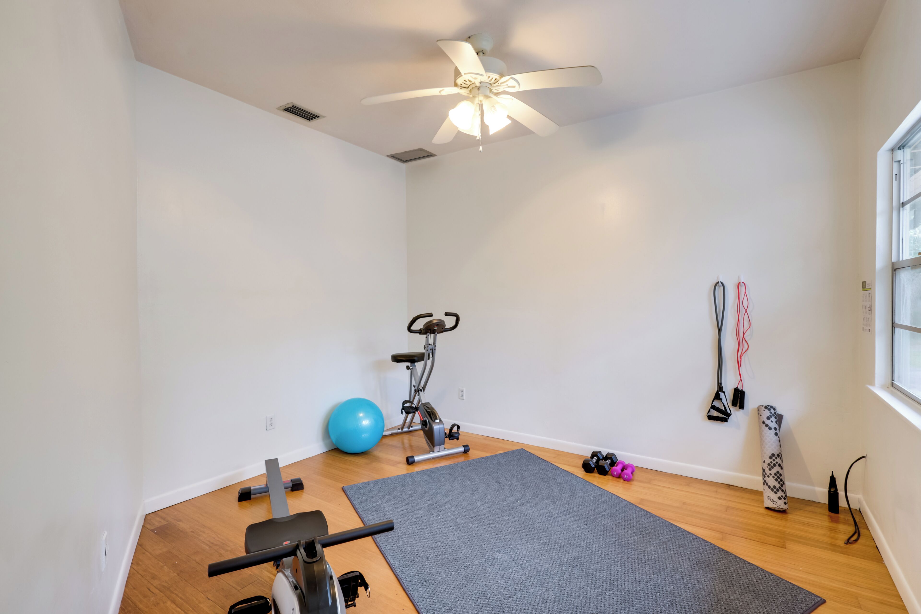 A room with a ceiling fan, exercise equipment, a yoga mat, and a window.