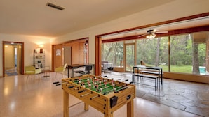 A spacious room with a foosball table, wooden flooring, large windows with a view of trees, and a ceiling fan. - Vacation Home Rental in Gainesville, Florida! (Gainesville)