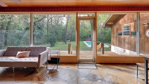 A spacious living room with a large sliding glass door leading to a wooden deck, a comfortable sofa, and a stone-tiled floor. - Vacation Home Rental in Gainesville, Florida! (Gainesville)