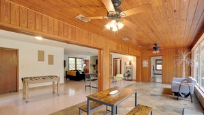 A spacious room with a wooden ceiling, stone flooring, a foosball table, a wooden table with benches, and a large window providing natural light. - Vacation Home Rental in Gainesville, Florida! (Gainesville)