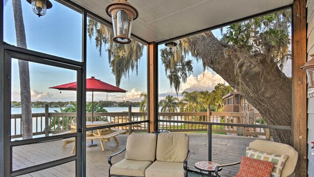 A covered outdoor seating area with a cushioned bench, a small table, and a red umbrella.