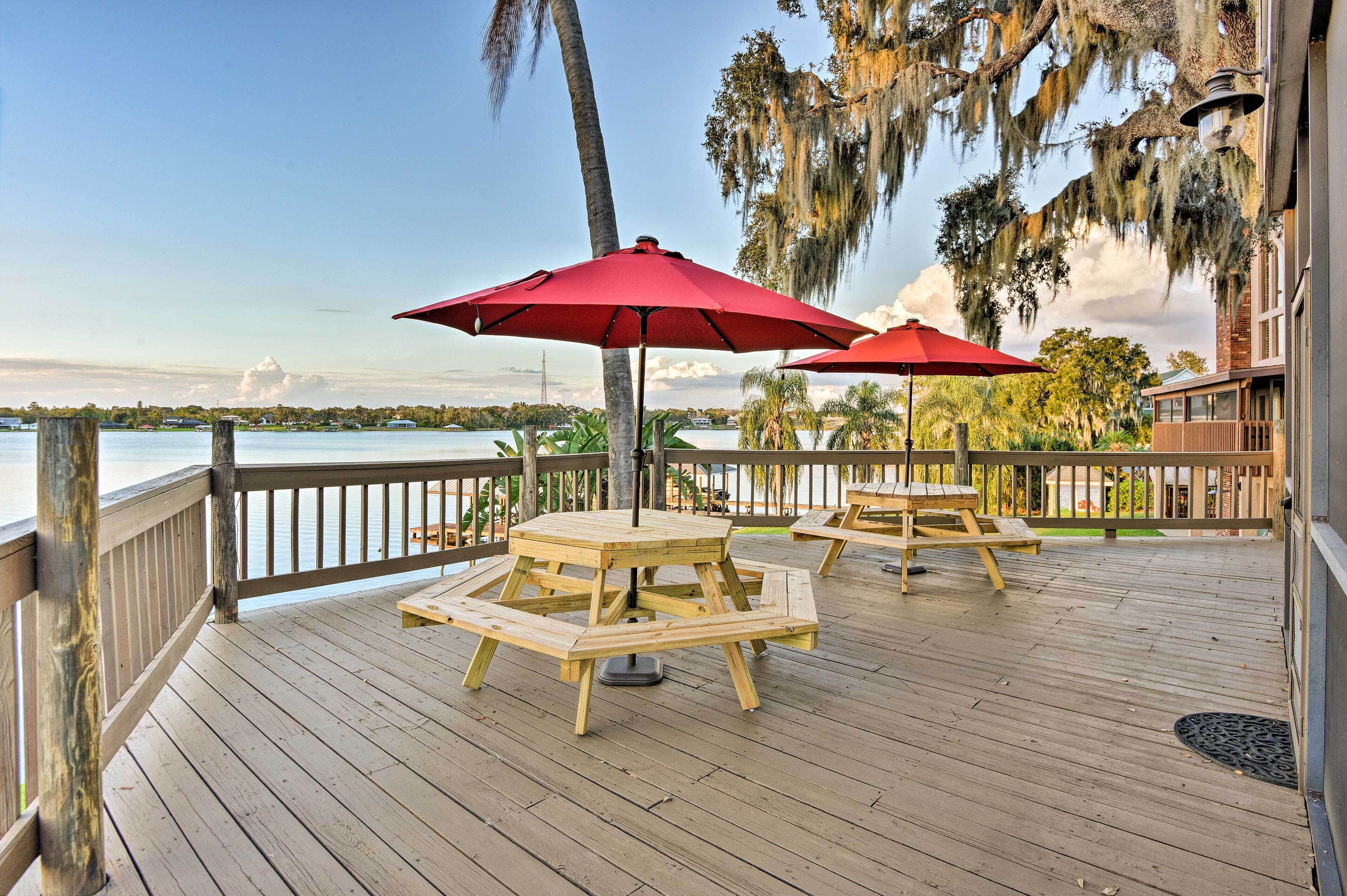 A wooden deck with picnic tables and red umbrellas overlooking a body of water.