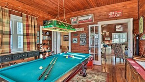 A pool table with cues and balls, wooden walls, and a plaid curtain.