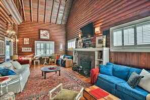 A log cabin interior with a fireplace, wooden walls, a large window, and a cozy seating area. - Lakefront Florida Retreat - Pool Table & Boat Dock (Lake Placid)