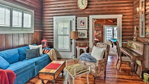 A log cabin interior with a blue sofa, a wooden piano, and a billiards table.