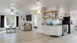 A spacious living area with a ceiling fan, a sofa, a coffee table, and a kitchen with white cabinets and a built-in oven.