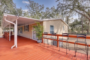 A covered porch with a railing, a potted plant, and metal chairs.