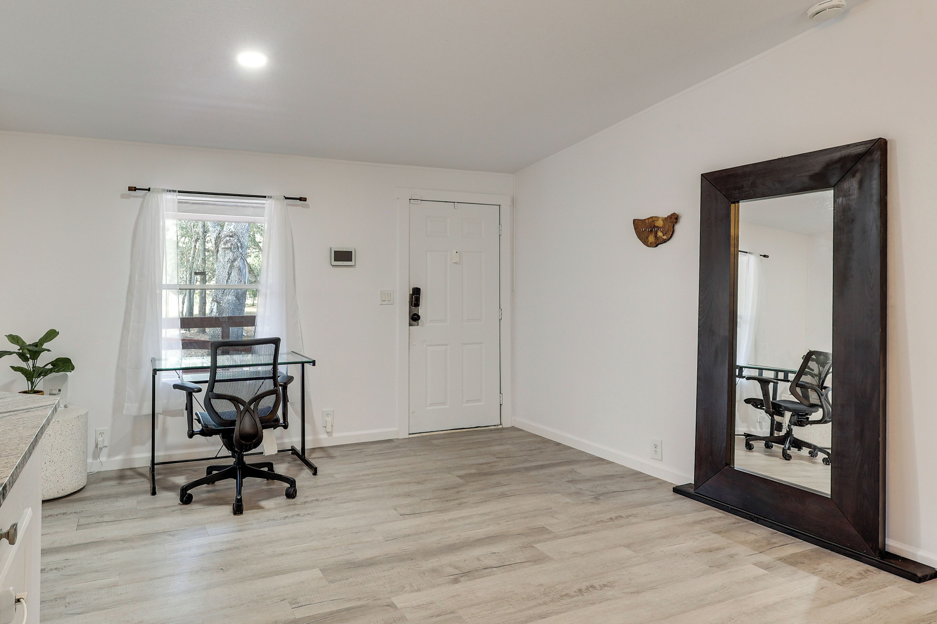 Une pièce avec un bureau en verre, une chaise, un grand miroir et une porte.