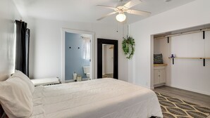 A bedroom with a bed, a ceiling fan, a radiator, a hanging plant, a wardrobe, and a bathroom visible through an open door.