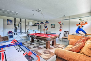 A room with a pool table, foosball table, and a sofa.