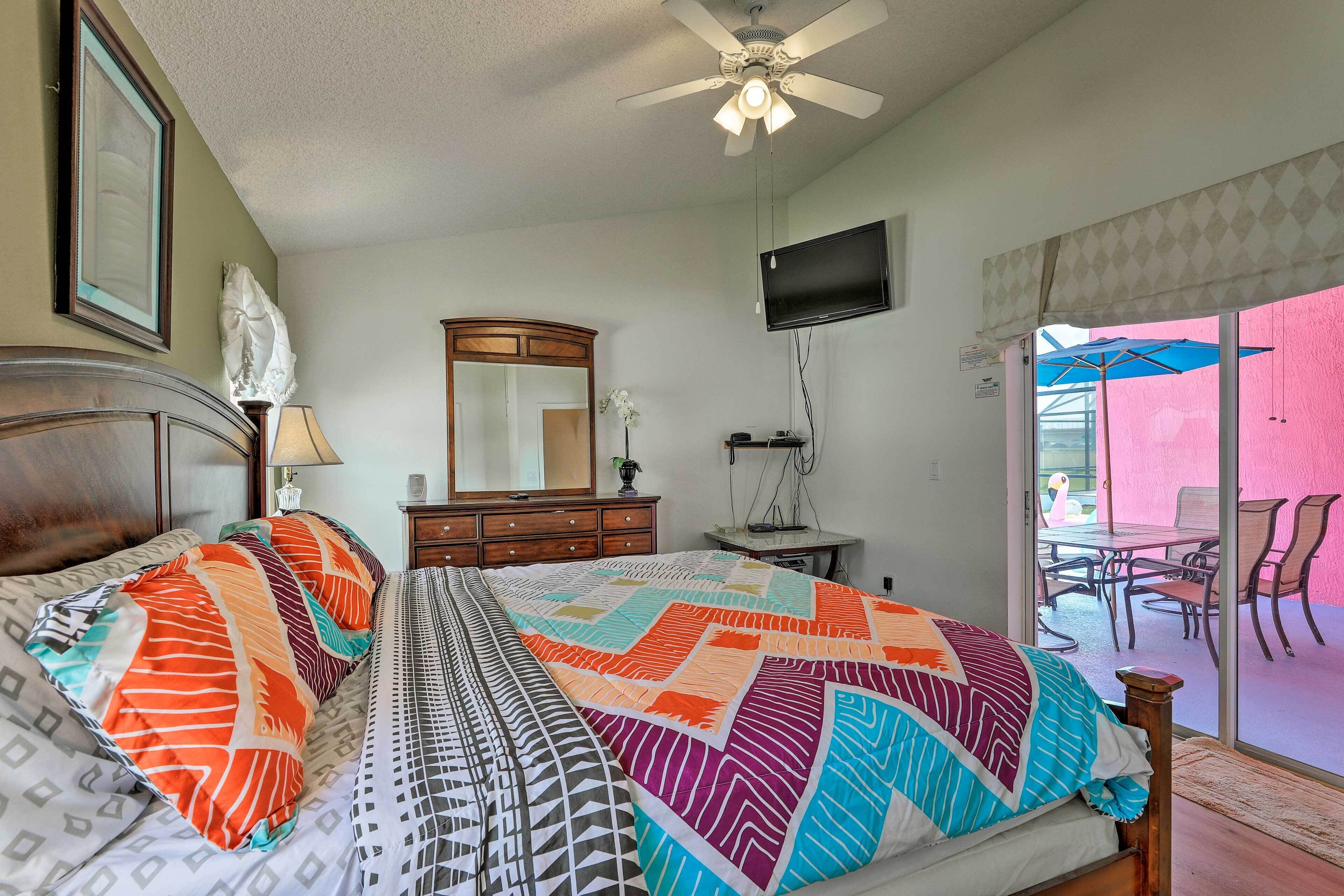Une chambre à coucher comprenant un lit, une commode, un miroir, une télévision et un balcon avec des chaises et un parasol.