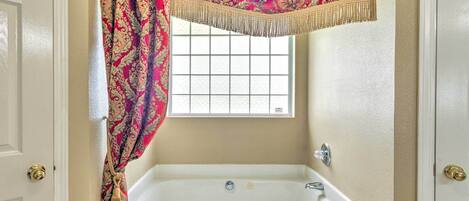 Casa de banho com uma banheira branca, uma janela com padrão quadriculado e uma porta com puxador de latão.