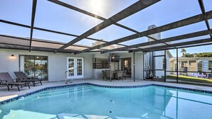 Une piscine intérieure dotée d’un toit en verre, de chaises longues et d’un espace patio avec des sièges extérieurs.