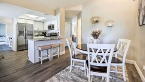 Une cuisine moderne avec des meubles blancs, un îlot central et un coin repas comprenant des chaises blanches et une table en marbre.