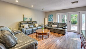 A spacious living room with leather sofas, a wooden coffee table, and large windows offering a view of greenery. - Dock & Beautiful Views! Spacious Bellows Lake Gem (Tampa)